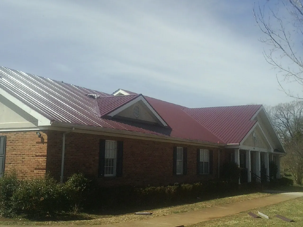 Red metal roof with gabled entries on a long brick building, from a Hail Damage Roof Repair job in Essex