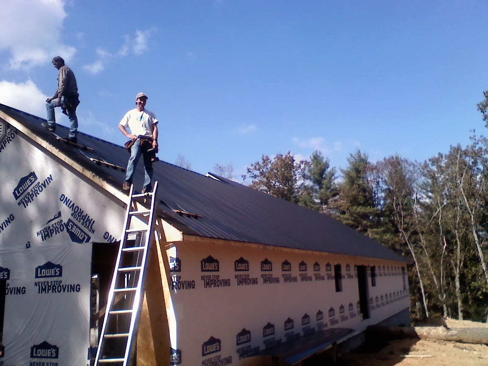 Two roofers standing on a long dark metal roof over a wrapped building in Essex
